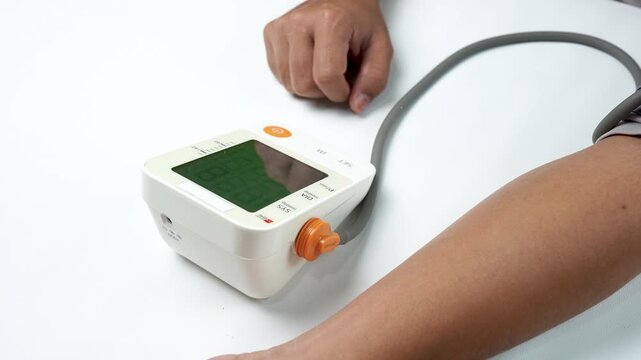 Close up of a person pressing the power button on a digital blood pressure monitor before measurement, highlighting home healthcare, medical device, heart health, wellness, and preventive care.