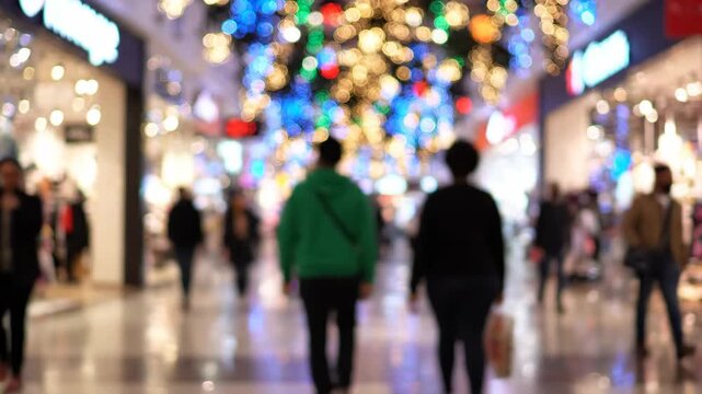 Blurred image of people walking inside a shopping mall with festive holiday lights in the background