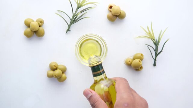 Slow motion video of hand pouring extra virgin olive oil into small glass bowl on white background