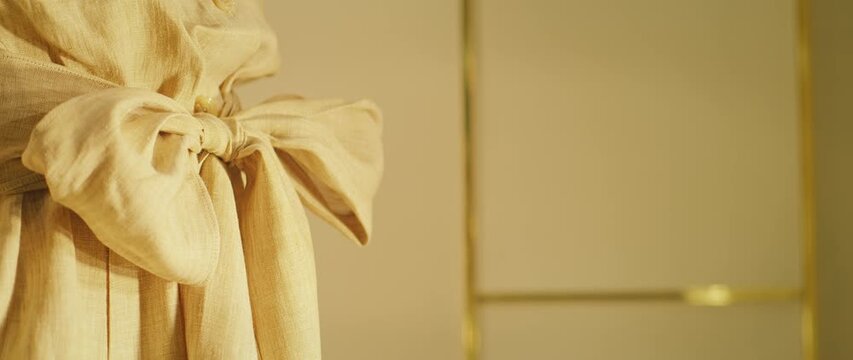 Closeup of yellow linen dress tied in a bow with golden wall in background