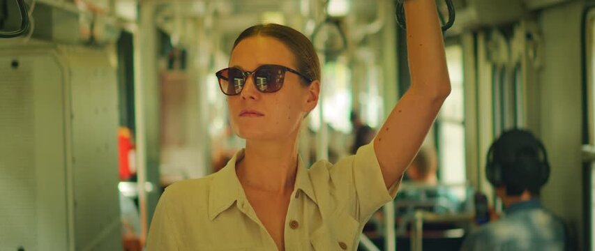 Woman standing on public transit holding strap while wearing sunglasses
