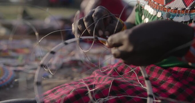 Close up of a Kenyan woman's hands assembling a traditional beaded wire necklace, slow motion.