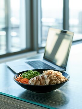 Healthy lunch bowl with chicken and laptop in office