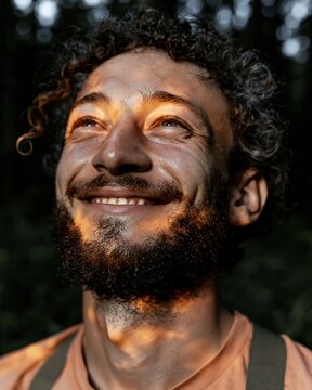Smiling man with curly hair gazing upward in a forest under warm golden morning light for outdoor mindfulness and adventure wellness themes