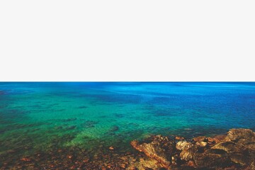 Vibrant turquoise sea with rocky shoreline under a clear sky. © Rawpixel.com