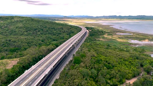 Aerial view of highway running along river and green hills. Transportation, infrastructure, travel and logistics concept