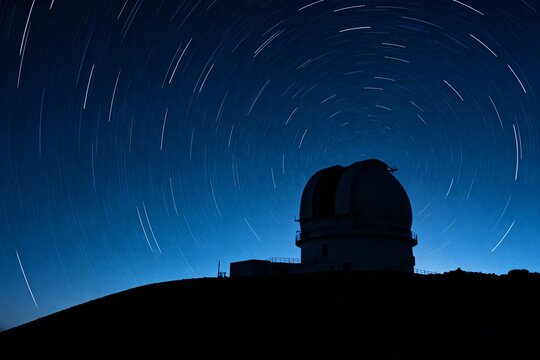Silhouette of an observatory dome under a star trail night sky