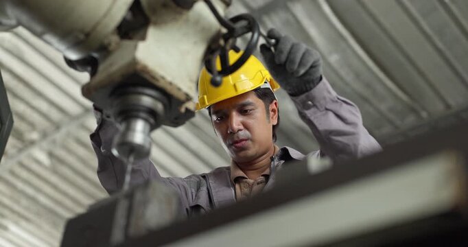 Factory worker operating industrial drilling machine to machine metal part in workshop