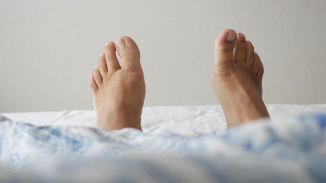 Feet of person waking up on bed with white and blue linen