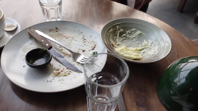 A close up view of an empty and dirty dinner plate and a soup bowl placed on a wooden table in an indoor restaurant