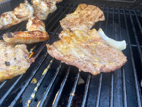 Steaks und H&auml;hnchenfl&uuml;gel auf dem Gasgrill w&auml;hrend eines sommerlichen BBQ. Grillen im Freien, saftiges Fleisch, Outdoor Cooking, Grillabend und mediterraner Lifestyle.