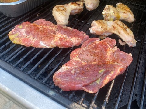 Steaks und H&auml;hnchenfl&uuml;gel auf dem Gasgrill w&auml;hrend eines sommerlichen BBQ. Grillen im Freien, saftiges Fleisch, Outdoor Cooking, Grillabend und mediterraner Lifestyle.