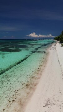 Vertical drone ascends over White Beach in Panglao, showing shallow turquoise water, reef flats, white sand, and beachgoers