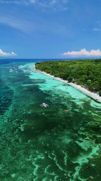 Vertical drone descends while tracking a longboat along White Beach, showing reef, clear water, and shoreline in Panglao