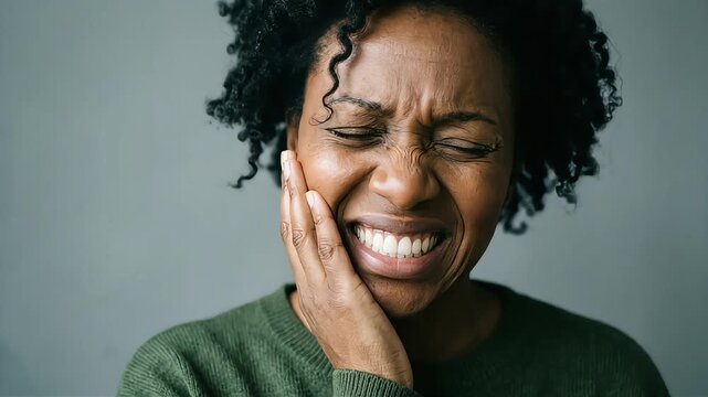 A young Black woman, suffering from a severe toothache, closes her eyes and clutches her cheek, her face contorted in agony.