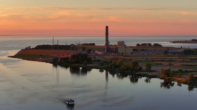 Ferry boat sailing near an industrial power plant at sunset