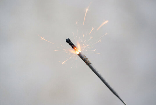 Close up of a lit sparkler stick with emerging sparks against a light grey background