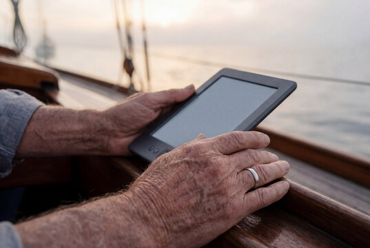 Senior person holding an electronic reader device while relaxing outside on a wooden boat