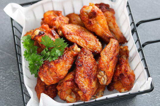 Top view of a pile of crispy fried chicken wings, topped with parsley garnish, served in a black wire serving basket lined with white paper.