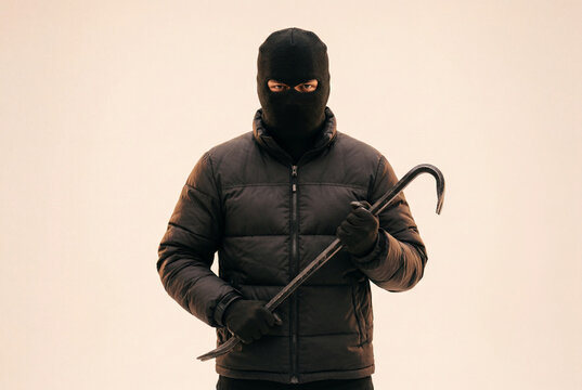 Dangerous criminal wearing a black balaclava and dark winter jacket holding a metal crowbar