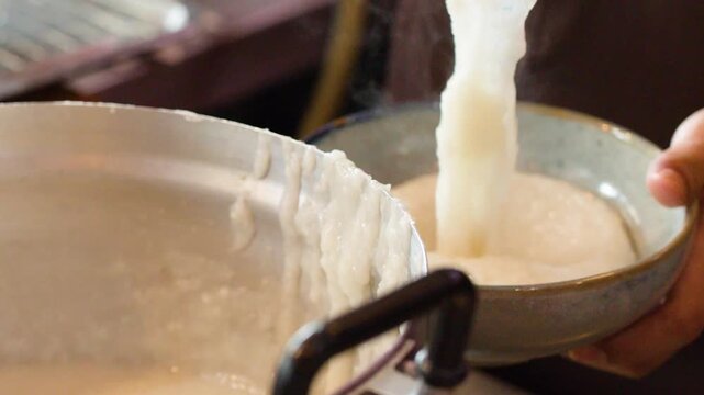 Chef Ladling Hot Rice Congee into a Ceramic Serving Bowl