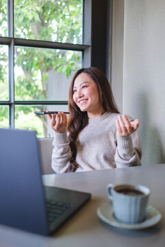 Vertical of a woman holding smart phone and using voice messaging, talking with ai assistant for Artificial intelligence concept while working on laptop