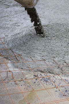 Wet cement pouring from a mixer truck chute onto a steel wire mesh for road