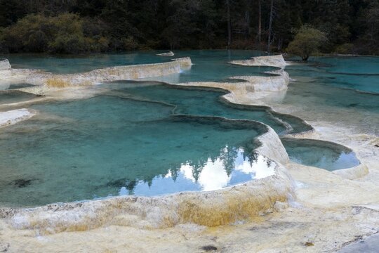 Natural travertine pools with clear turquoise water and mineral deposits in a forested area