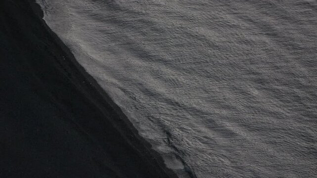 Black sand, ocean waves, coastline A mesmerizing aerial abstract view of dark black volcanic beach meeting the sea
