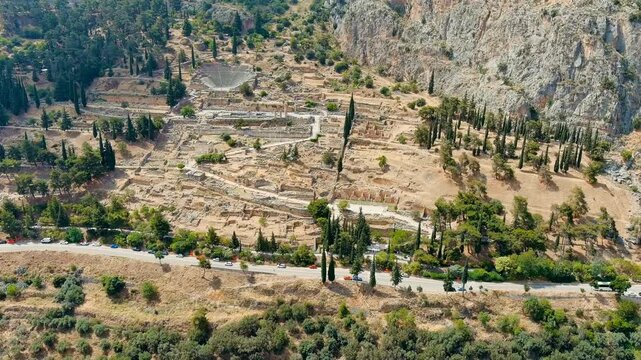 Delphi, Greece. Drone footage over the sanctuary ruins on Mount Parnassus, with the theater and temple foundations amid dry summer terrain and steep limestone cliffs. Drone footage, Departure of the 