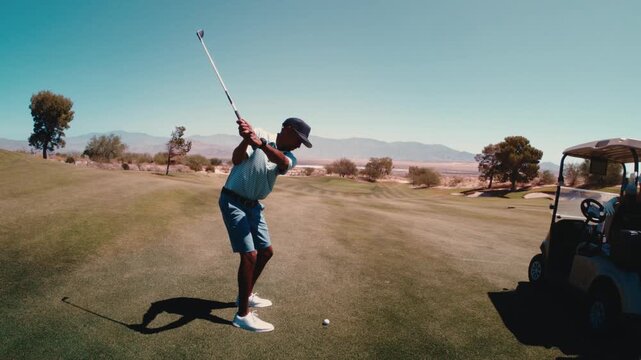 Black golfer hits crisp iron shot from fairway in ultra slow motion as the camera tilts down, desert mountains golf course behind, 4k 800 fps in summer