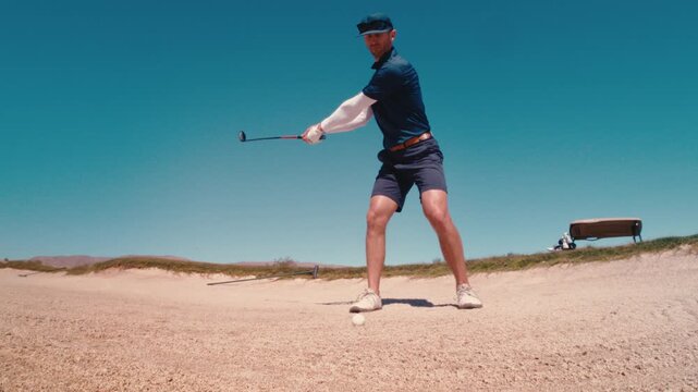 Scratch golfer hits hybrid out of fairway bunker, spraying sand at camera, 4k 800fps ultra slow motion on sunny summer day