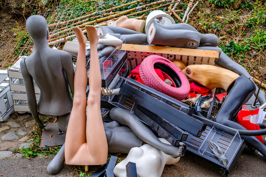 Discarded mannequins and various items clutter a hillside area during daylight, showcasing a blend of urban waste and forgotten objects