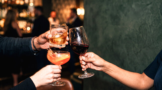 Cheers to Friendship: Three hands clink their glasses filled with cocktails and wine in a toast, celebrating a special moment or a casual get-together in a stylish bar atmosphere.