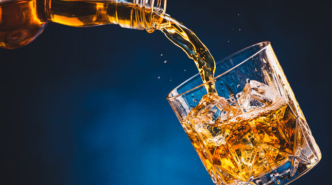Amber Spirit Pour: A stream of golden whiskey cascades from a glass bottle, splashing into a crystal tumbler filled with ice, creating a dynamic and inviting beverage scene.