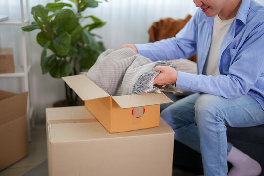 Asian man unpacking bubble wrap from cardboard box while relocating to new apartment with copy space