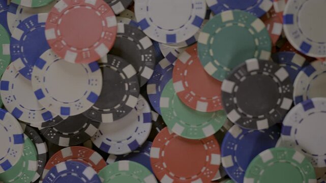 Horizontal 4K video panning across scattered red, green, blue, black and white poker chips creating a colorful casino gaming background.