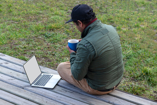 Digital nomad relaxing outdoors with a hot drink and blank screen computer, horizontal shot