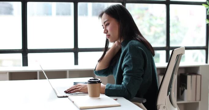 Asian woman feeling excitement and celebrating achievement while reading good news on a laptop computer, working remotely from her modern home office space