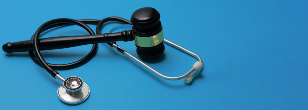 Serious medical malpractice concept features black stethoscope and wooden judge gavel on blue background symbolizing legal justice concern