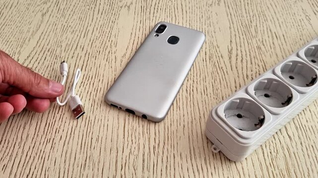 Smartphone, USB cable, and power strip arranged on wooden surface, highlighting everyday tech setup, charging accessories, and modern connectivity in a simple scene