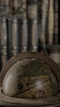 Vertical 4K video of an antique-style globe spinning on a wooden stand with warm lighting and blurred library books in the background.