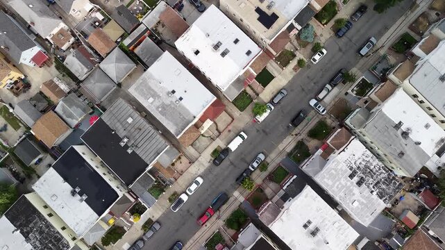 Aerial drone footage flying over the rooftops of a densely populated urban residential area in an american city, showing houses, backyards, streets, parked cars, and green trees