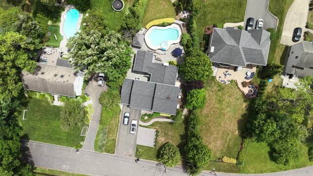 Aerial top down view flying over a quiet american suburban neighborhood with beautiful homes, lush green lawns, private swimming pools, and tree lined streets on a sunny summer day