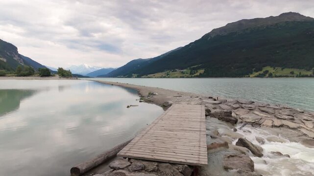 Panoramic pan left of Lake Reschen ending at the bell tower of the church remains from the flooded village Graun - Curon in Val Venosta, South Tyrol, Italy