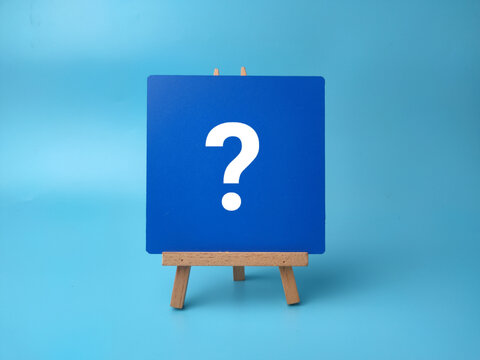 A small wooden easel stands on a blue surface, supporting a blue square board with a white question mark