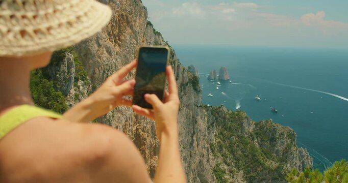 Woman photographing Capri seascape with Faraglioni sea stacks from a high scenic cliff viewpoint