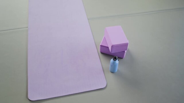 Yoga mat, foam blocks, and water bottle resting on floor during slow camera movement. Minimalist fitness equipment setup is ideal for promoting wellness, pilates, and healthy lifestyle brands