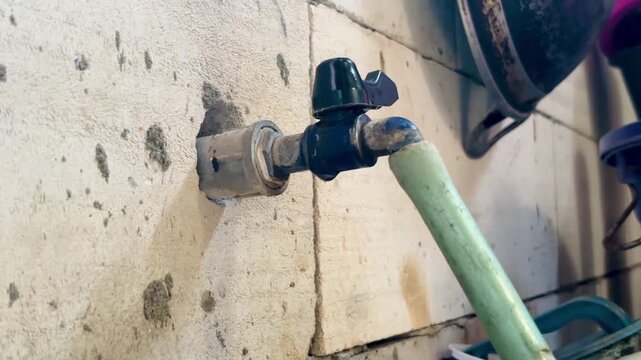 Leaking water faucet with slow dripping water attached to a household wall. Close-up showing water waste, plumbing maintenance, home repair, conservation, and everyday utility concept.