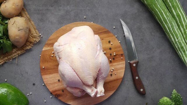 Raw whole chicken on wooden board with various fresh vegetables and spices on dark background top view, fresh food for cooking